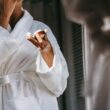 Recorte mujer étnica anónima en suave bata de baño aplicando crema nutritiva en la cara mientras se refleja en el espejo en casa