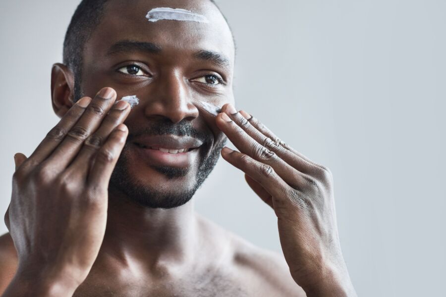 Hombre sonriente aplicando crema facial como parte de su rutina diaria de cuidado de la piel para una piel sana.