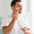 generame un hombre poniendose creama en la cara y tiene un tarro de crema en la mano