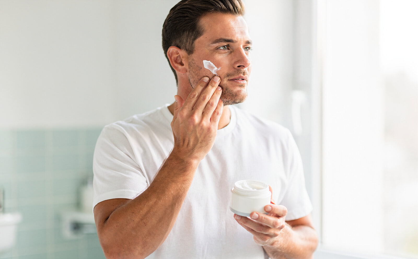 generame un hombre poniendose creama en la cara y tiene un tarro de crema en la mano