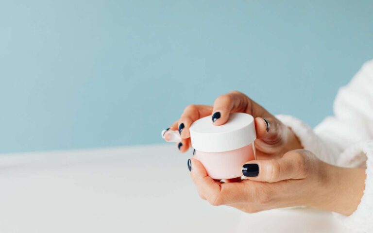 Imagen de cerca de las manos sosteniendo un frasco de crema para el cuidado de la piel, centrándose en productos de belleza y cuidado personal.