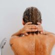 Vista trasera de una mujer disfrutando de una ducha fresca, con agua corriendo por su espalda.