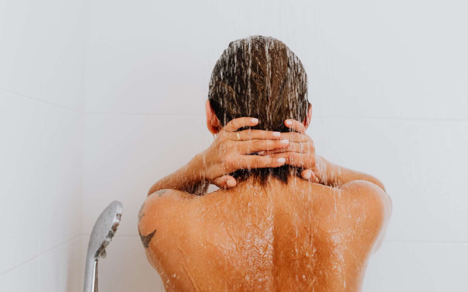 Vista trasera de una mujer disfrutando de una ducha fresca, con agua corriendo por su espalda.