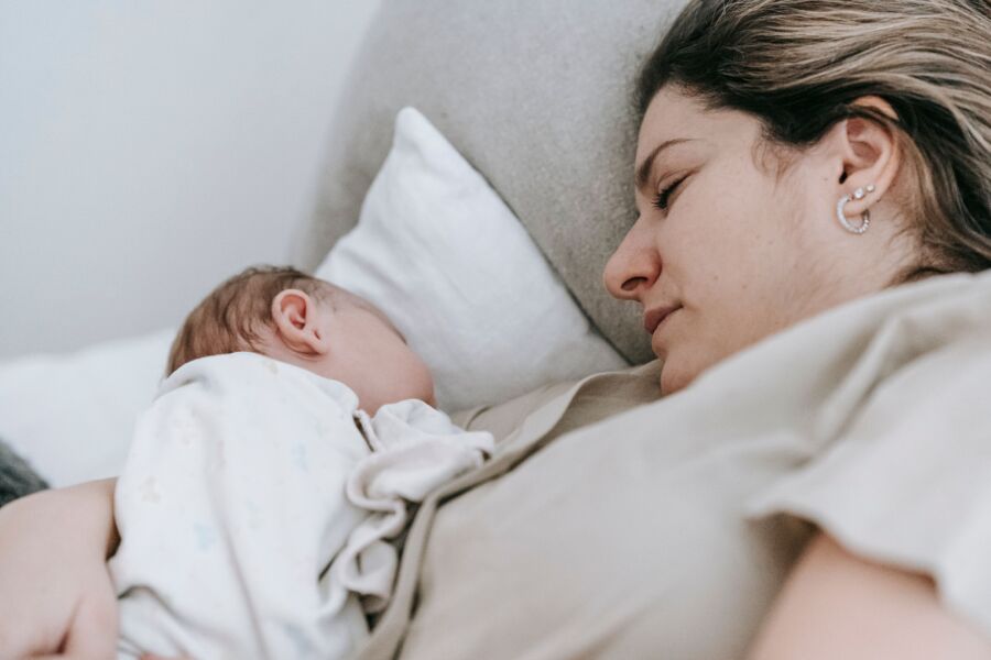 Vista lateral de una madre cariñosa con un lindo bebé recién nacido en brazos durmiendo tranquilamente en una cama cómoda en un dormitorio ligero en casa
