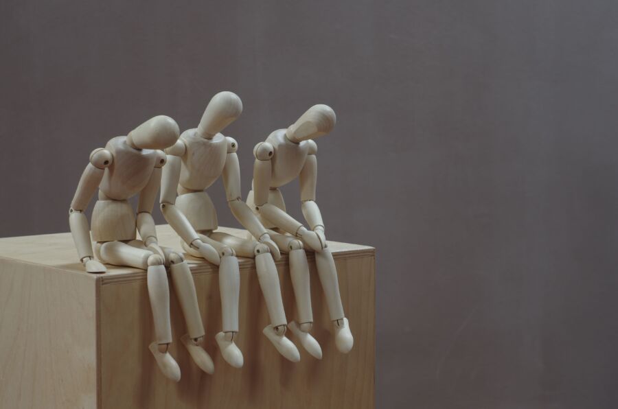 Tres maniquíes de madera en poses pensativas sobre un bloque de madera sobre un fondo neutro.