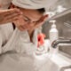 Mujer hermosa joven en el baño con una toalla en la cabeza se lava la cara con agua del grifo