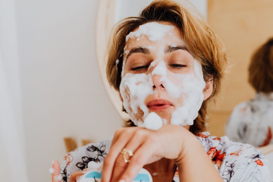 Primer plano de una mujer aplicando un lavado facial espumoso, que abarca el autocuidado en interiores.