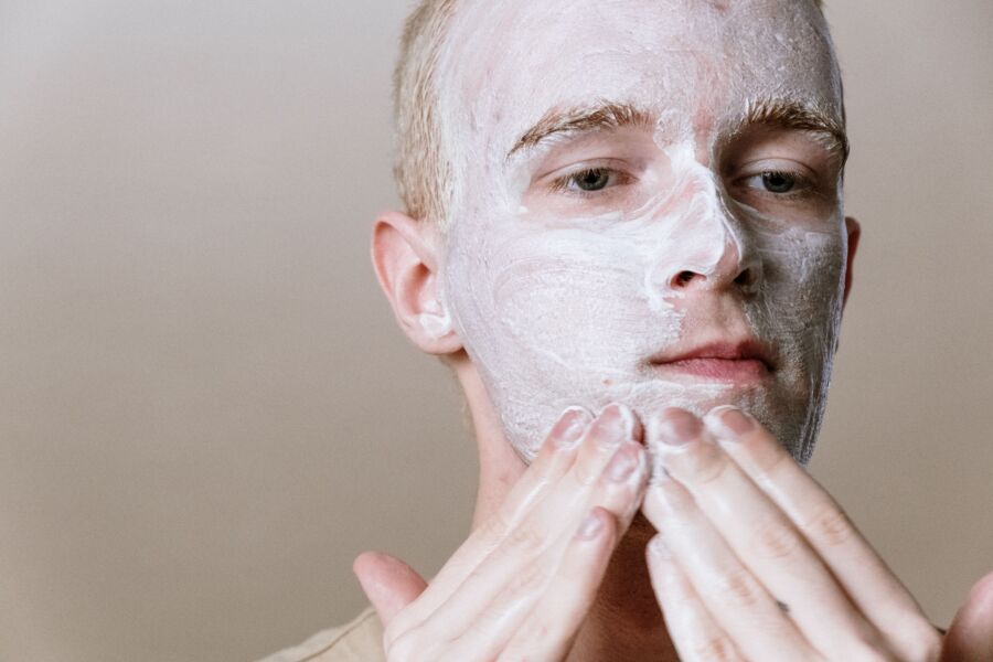 Primer plano de un hombre aplicando un limpiador facial para una rutina refrescante de cuidado de la piel, centrándose en el autocuidado y la salud.