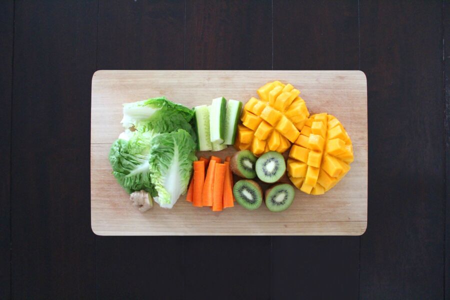 Frutas y verduras frescas preparadas para una ensalada saludable en una tabla de cortar de madera.