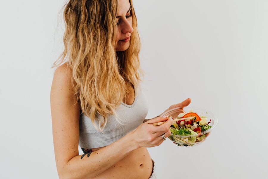 Una mujer caucásica en un sostén deportivo disfrutando de una ensalada fresca, encarnando la alimentación y estilo de vida saludables.