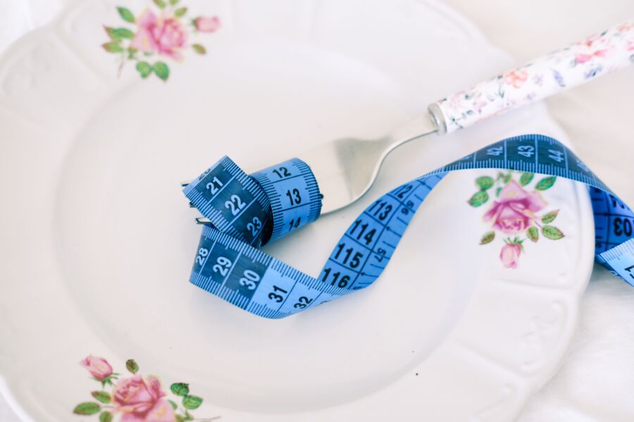 Un plato floral con un tenedor y cinta métrica azul que simboliza la dieta o la alimentación saludable.
