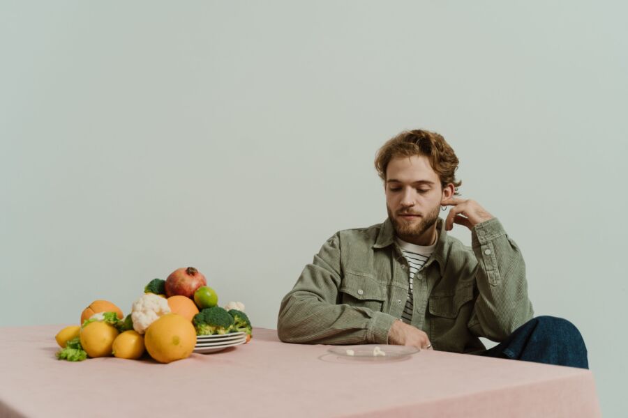 Un hombre con atuendo informal se sienta en una mesa con varias verduras, evocando un estado de ánimo reflexivo.