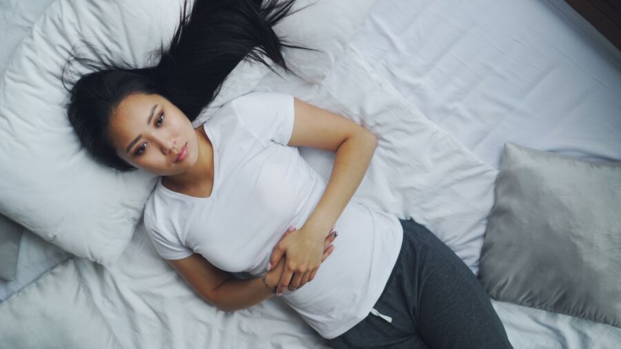 Una joven con atuendo informal yace en una cama blanca, con un aspecto relajado y pensativo.