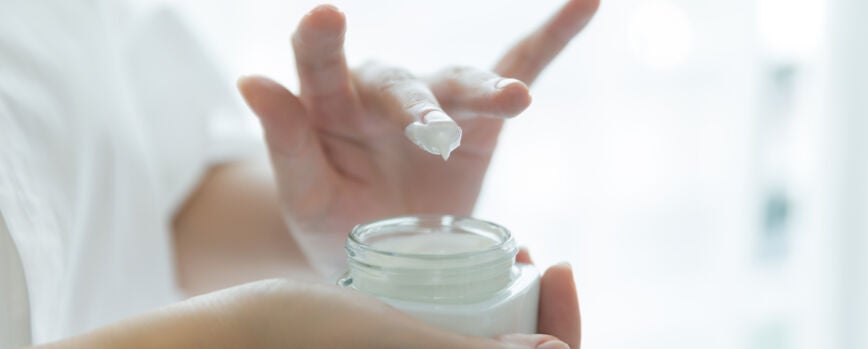 mujer sostiene un frasco con una crema cosmética en sus manos