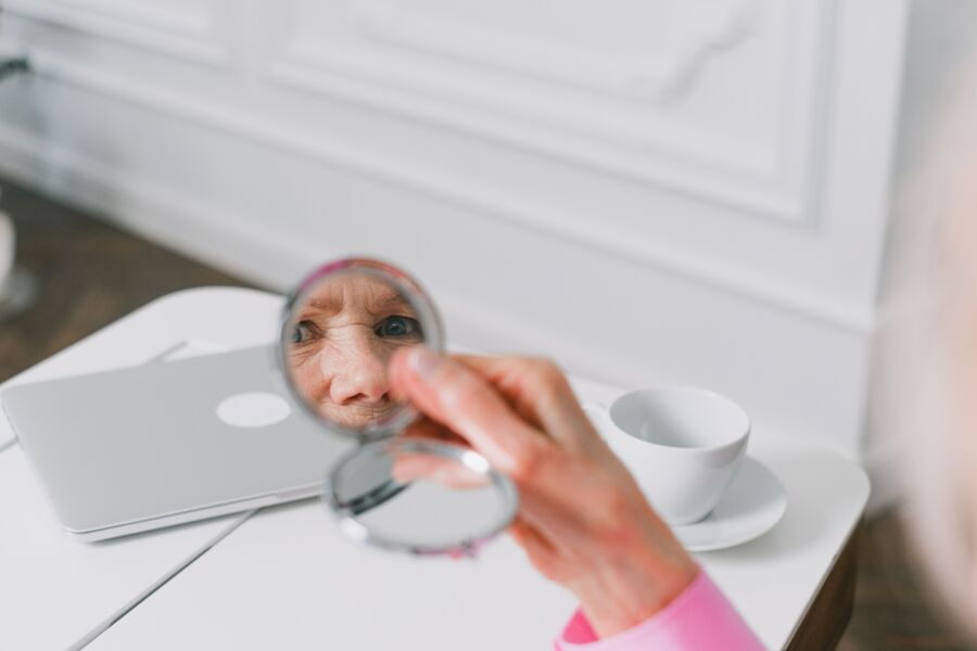 Primer plano de una mujer mayor sosteniendo un espejo de bolsillo, reflejando su rostro en el interior.