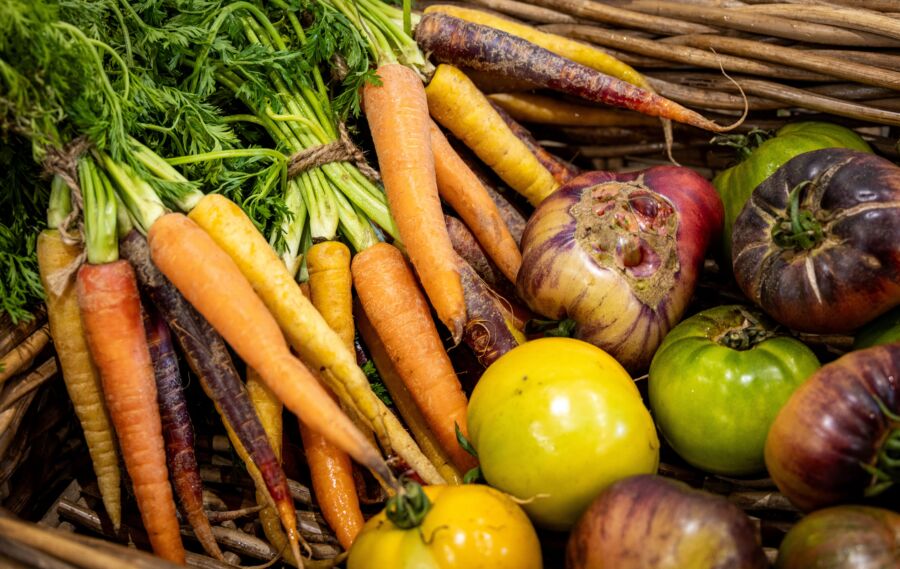 Primer plano de diversas verduras de la herencia, como zanahorias y tomates, en una cesta rústica de mimbre.