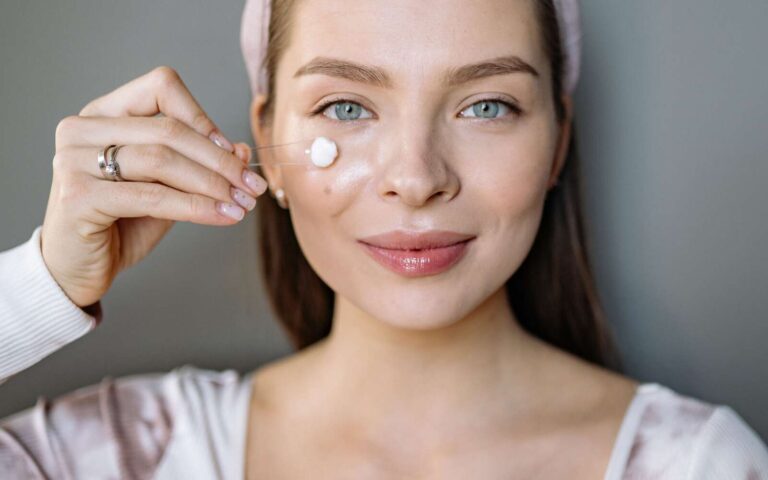 Mujer sonriente aplicando crema facial para la rutina de cuidado de la piel