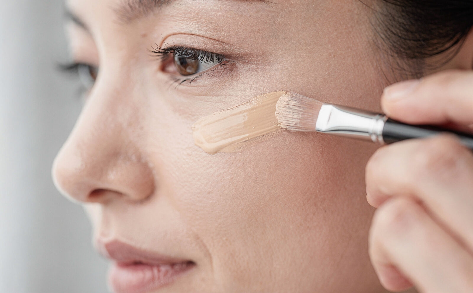 Persona genérica aplicando corrector con dedo o brocha en contorno de ojos, producto visible, sin foto de antes/después del resultado