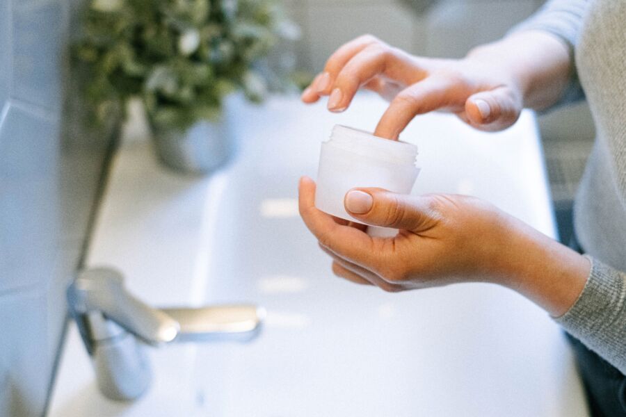 Primer plano de las manos de la mujer aplicando crema facial, enfatizando la rutina de autocuidado.