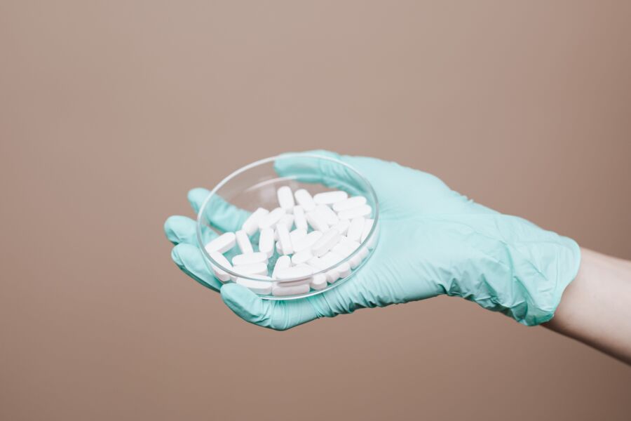 Una mano enguantada sosteniendo una placa de Petri llena de píldoras blancas en un entorno de atención médica.