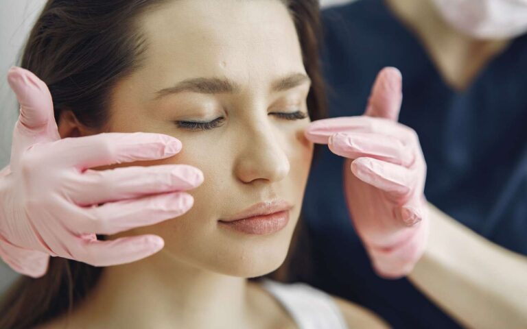 Primer plano de una mujer con los ojos cerrados recibiendo atención facial en una clínica de belleza en el interior.