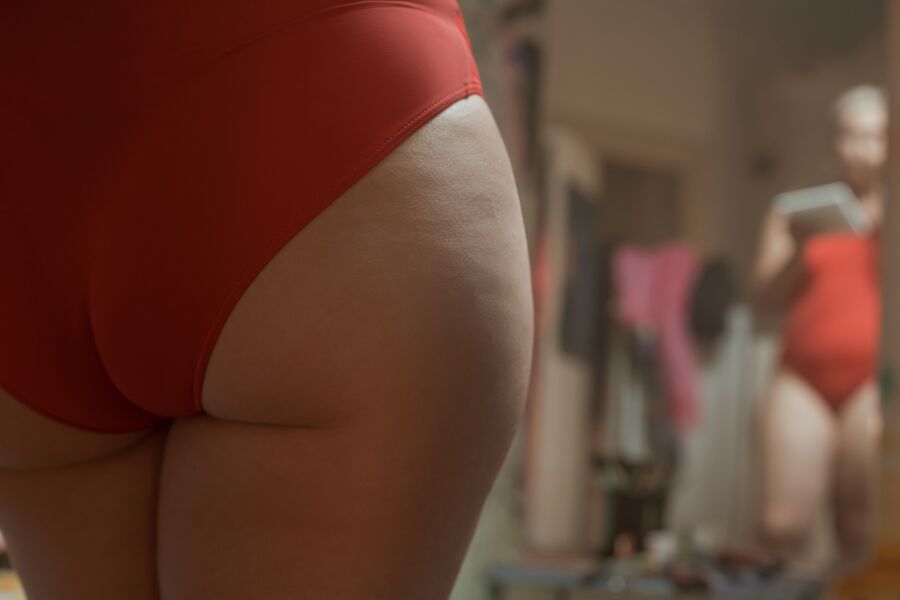 Una vista cercana de una persona que abraza la positividad corporal en traje de baño rojo, autorreflectante en un espejo.