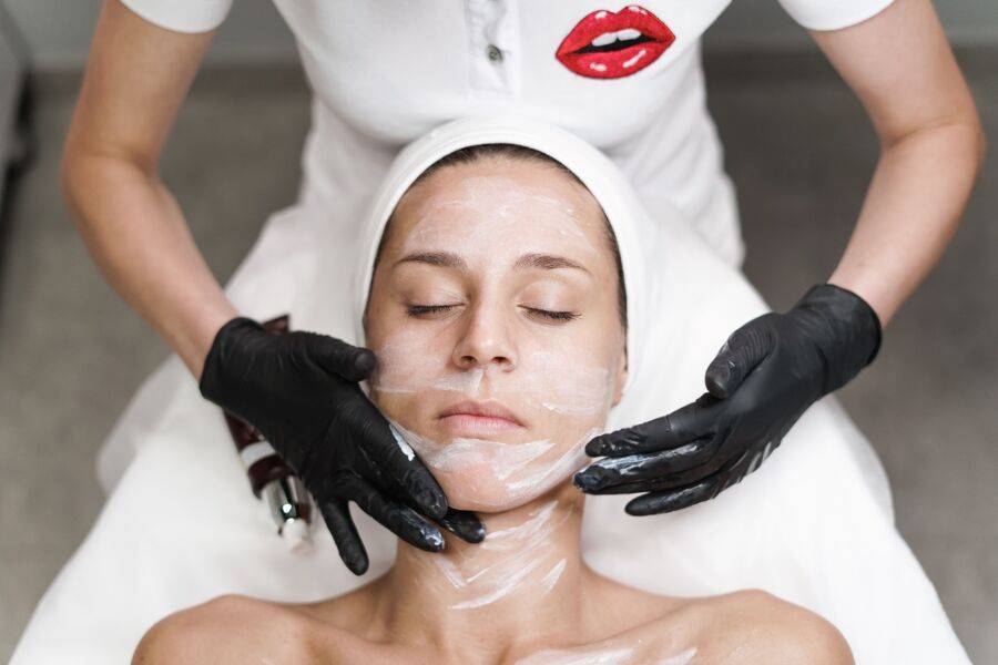 Mujer recibiendo tratamiento facial en spa, con esteticista aplicando mascarilla en un ambiente relajante.