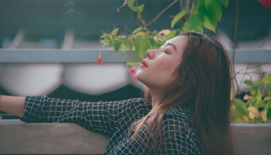 Una joven disfrutando de un momento de paz al aire libre con los ojos cerrados, rodeada de vegetación.