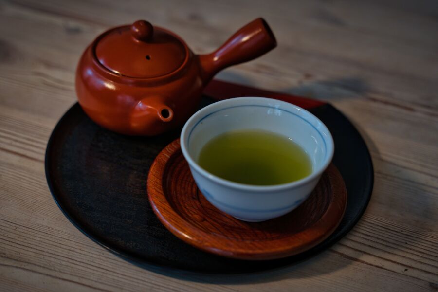 Tetera y taza de cerámica con té verde en una bandeja de madera, evocando la cultura japonesa.