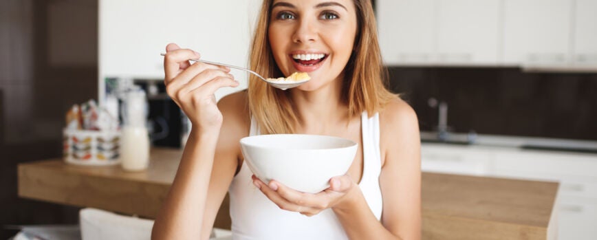 Foto de atractiva jovencita comiendo copos de maíz con leche en la cocina