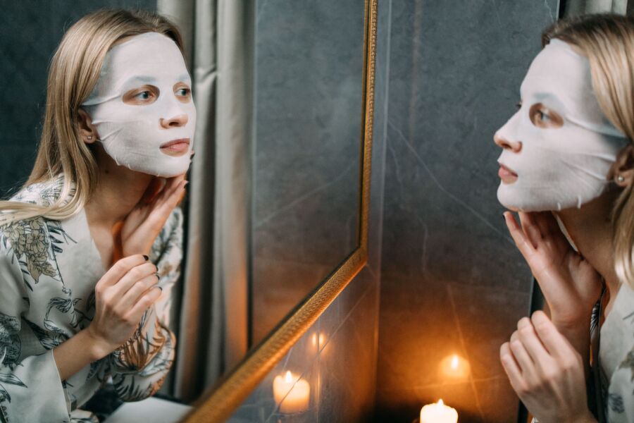 Mujer aplicando una mascarilla hidratante mientras se mira al espejo, creando un ambiente sereno y relajante.