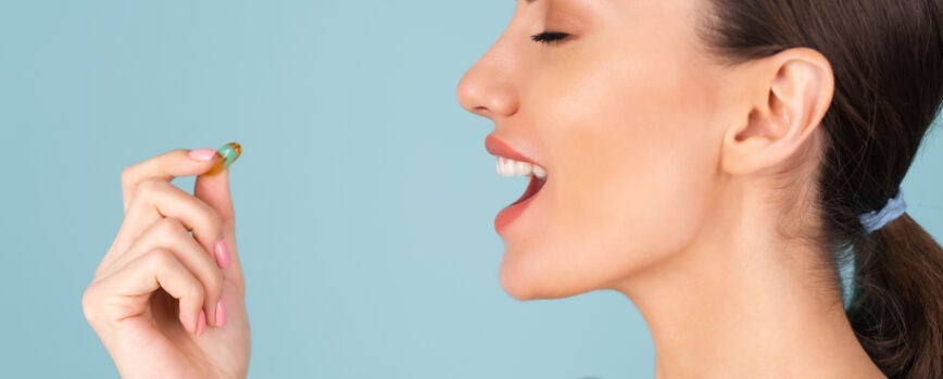 Retrato de belleza de primer plano de una mujer en topless con piel perfecta y maquillaje natural, sosteniendo un suplemento, vitamina omega 3, aceite de pescado, sobre un fondo turquesa