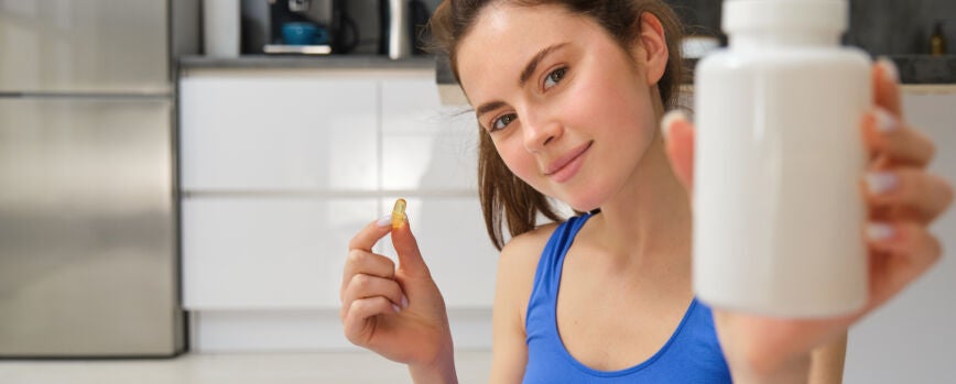 Primer plano retrato de una joven instructora de fitness mostrando una botella de vitaminas tomando cogollos