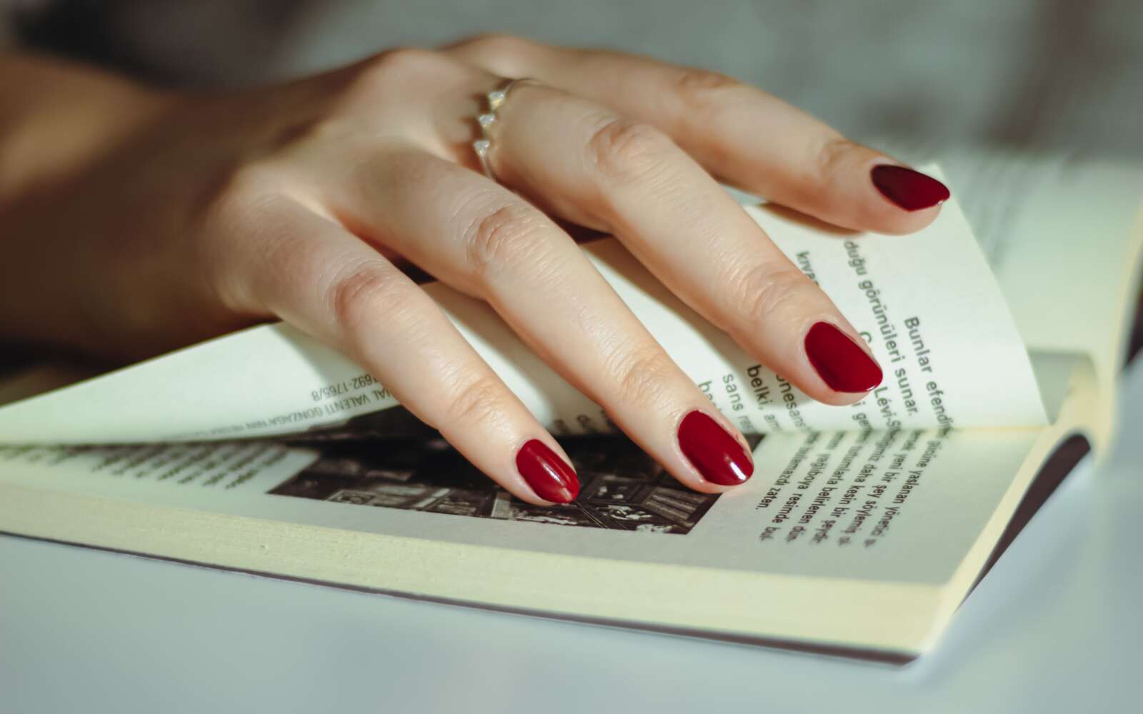 Una mano con esmalte de uñas rojo hojeando las páginas de los libros, simbolizando la lectura y la literatura.