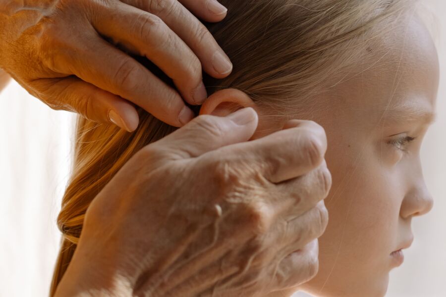 Un primer plano de una mano anciana arreglando el cabello rubio de una niña en el interior, destacando el vínculo multigeneracional.
