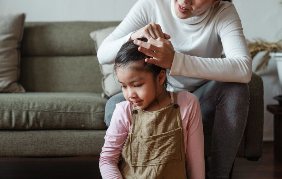 Una madre ata cariñosamente el cabello de su hija mientras está sentada en el sofá, compartiendo un tierno momento de unión.