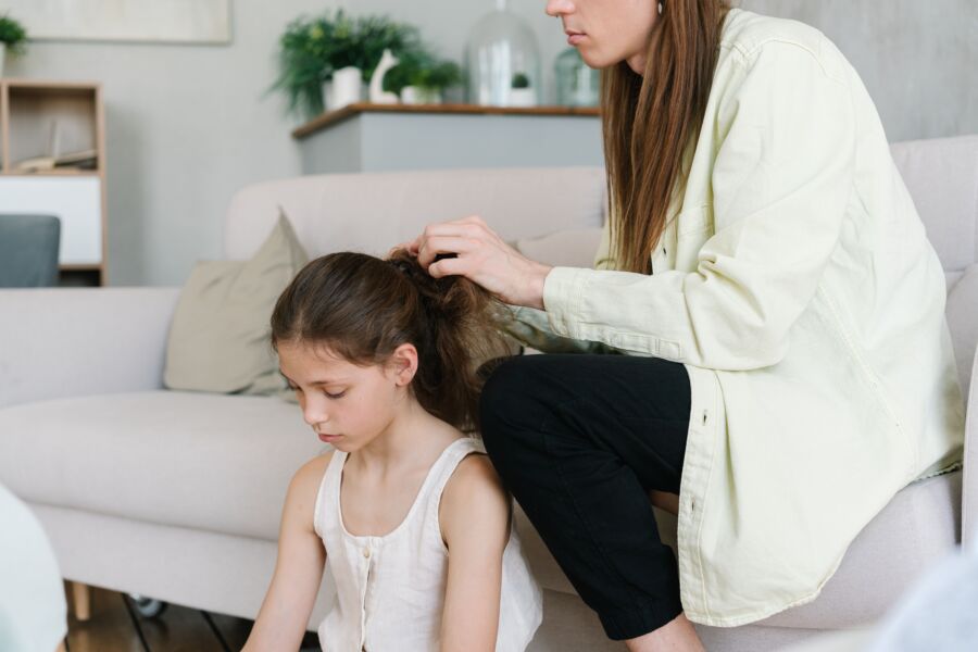 Una madre modela suavemente el cabello de su hija mientras está sentada en un sofá en una acogedora sala de estar.