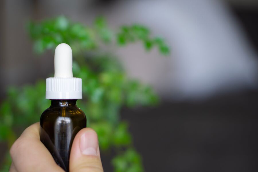 Mano sosteniendo una botella cuentagotas de aceite de CBD contra un fondo botánico de enfoque suave.
