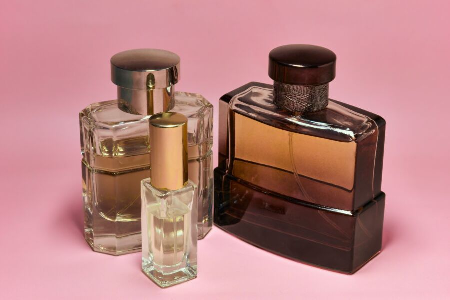 Tres elegantes frascos de perfume con elegantes tapas sobre un fondo rosa, que capturan una sensación de lujo y sofisticación.