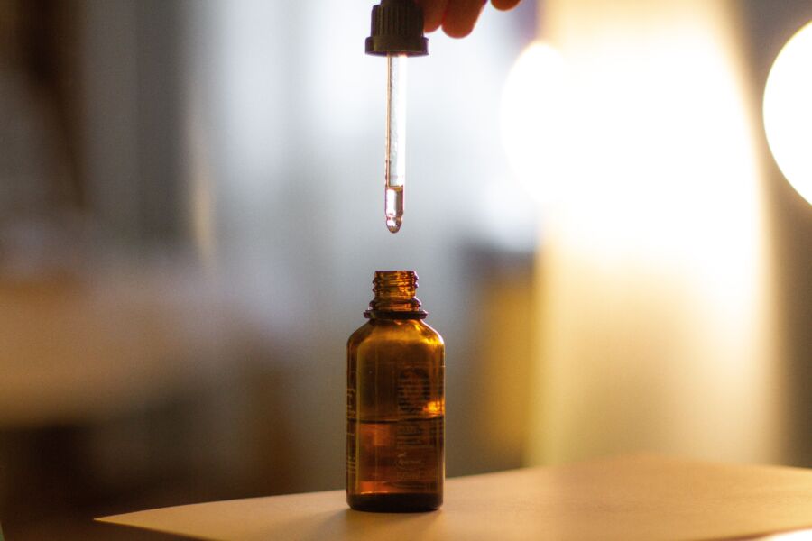 Primer plano de un cuentagotas de suero sobre una botella de color ámbar, con un fondo borroso suave y una luz brillante.