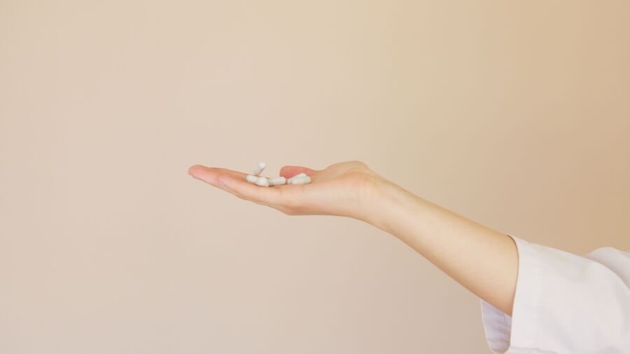Vista lateral de una farmacéutica irreconocible en uniforme blanco con una pila de analgésicos blancos en la palma contra un fondo marrón claro