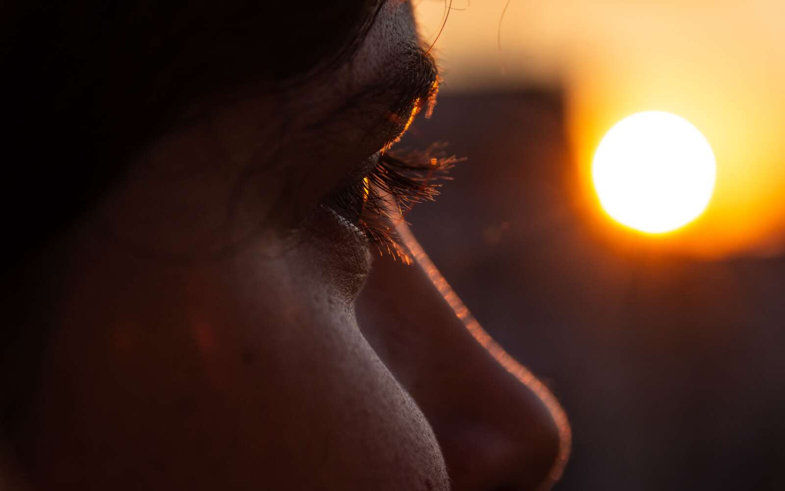 Un primer plano cautivador del ojo de una persona con una puesta de sol vibrante en el fondo, creando un ambiente cálido e introspectivo.