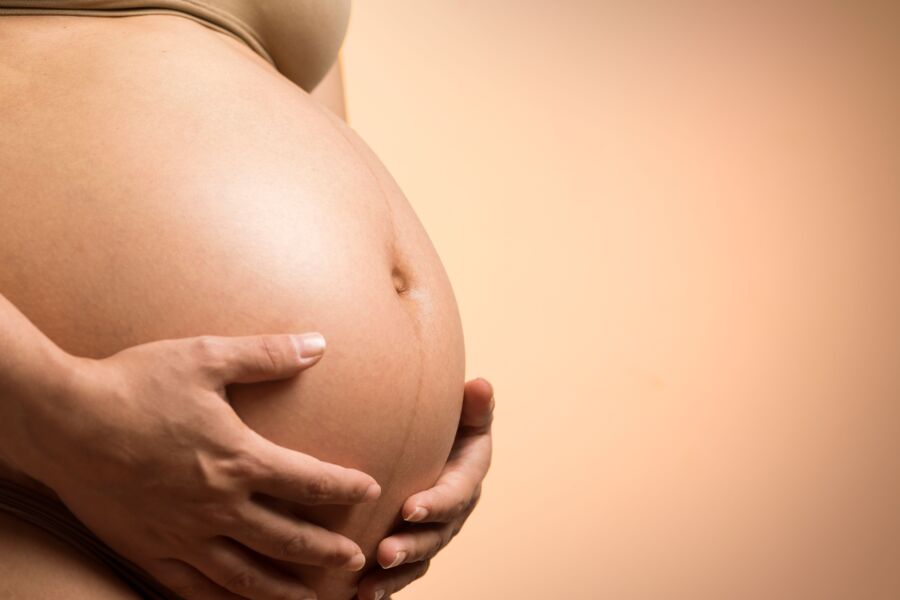 Un tierno primer plano de las manos de una mujer embarazada sosteniendo su vientre, simbolizando la maternidad y el amor.
