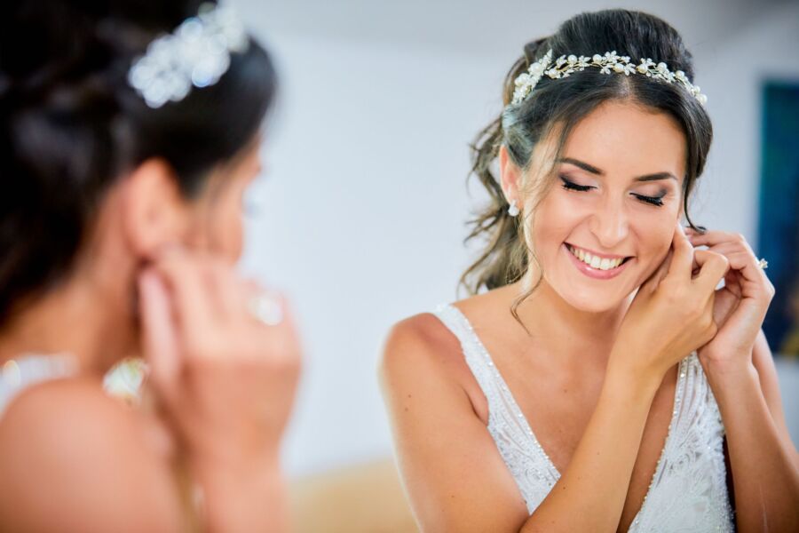 Una novia sonriente ajusta sus pendientes en una pose elegante, irradiando felicidad y belleza.
