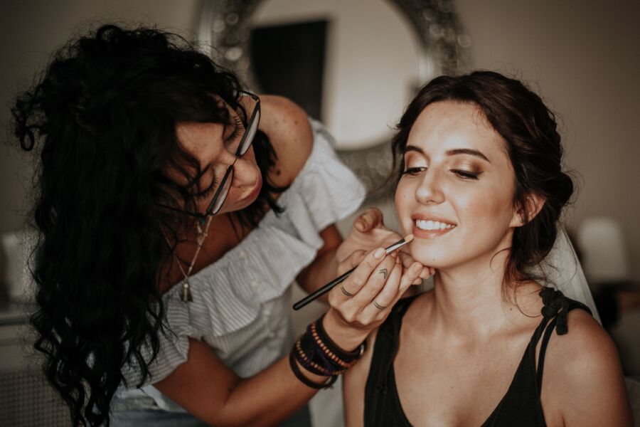 Un maquillador aplica hábilmente lápiz labial a una mujer sonriente en un entorno interior.