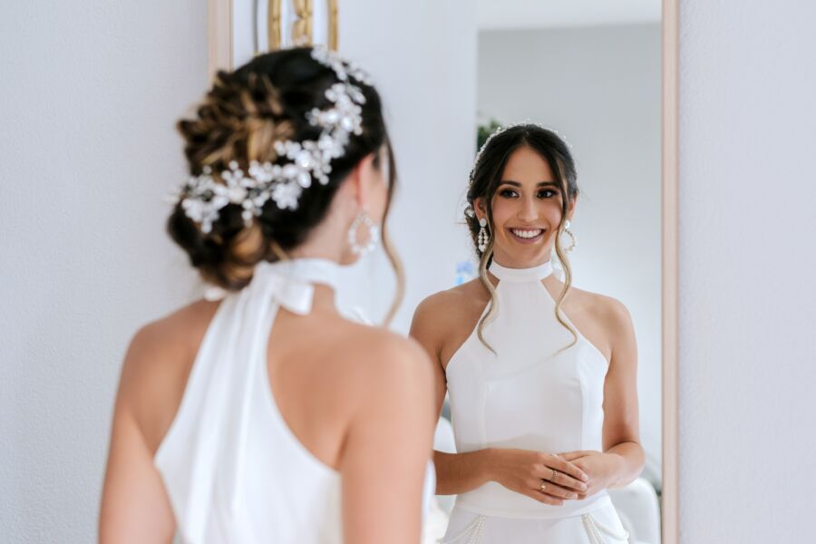 Elegante novia con un vestido blanco sonriendo a su reflejo en el hotel de Lisboa.