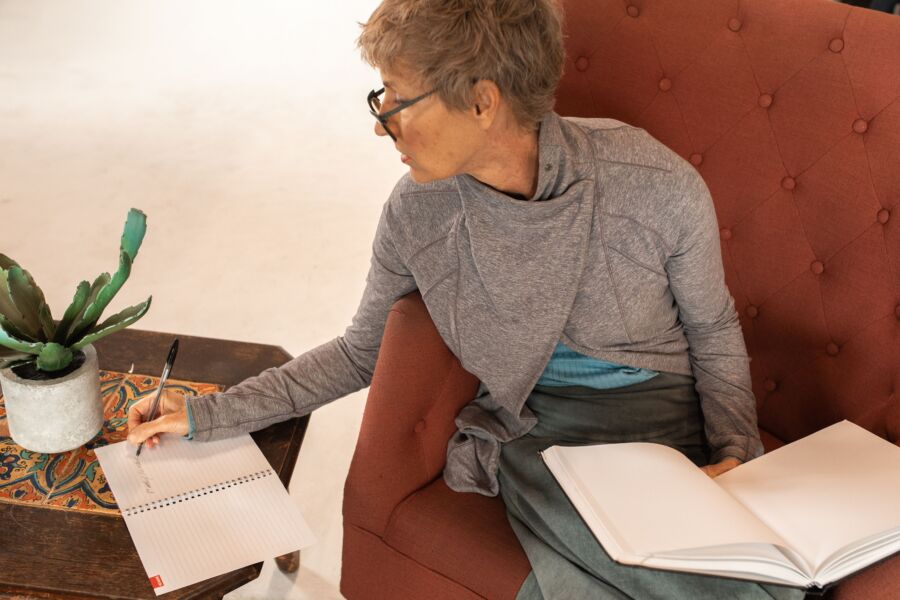 Mujer mayor escribiendo notas con un cuaderno mientras está sentada cómodamente en el interior.