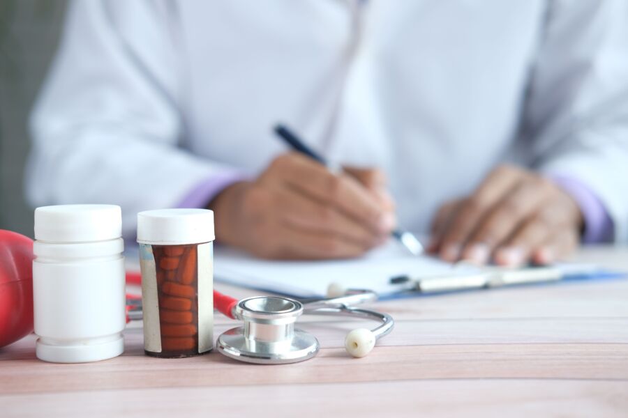 Primer plano del médico escribiendo la receta con medicamentos y estetoscopio en el escritorio.