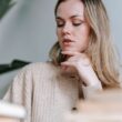 Cultivo inteligente serio hembra con pelo largo en cárdigan de lana beige cerca de un montón de libros borrosos