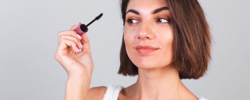Hermosa mujer con maquillaje mantenga pincel de rímel negro sobre pared gris, concepto de belleza
